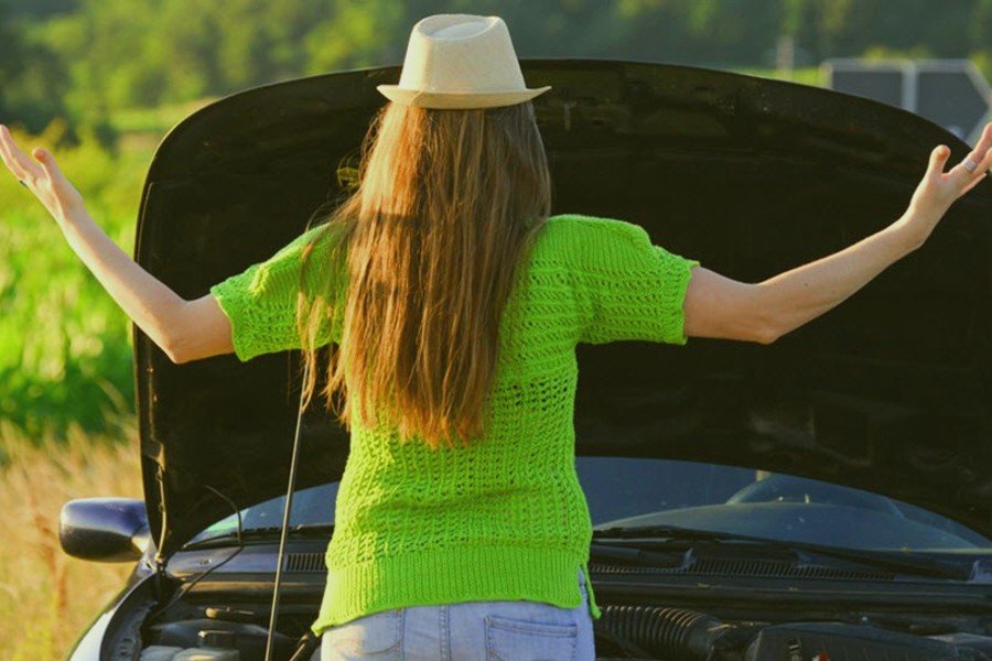 Photo of woman in front of her broken down car with the hood up.